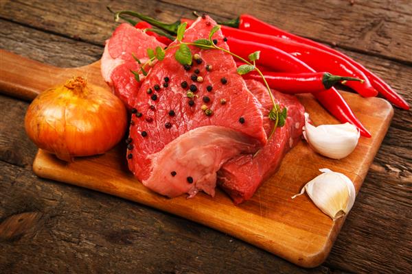 گوشت خام و سبزیجات روی میز چوبی