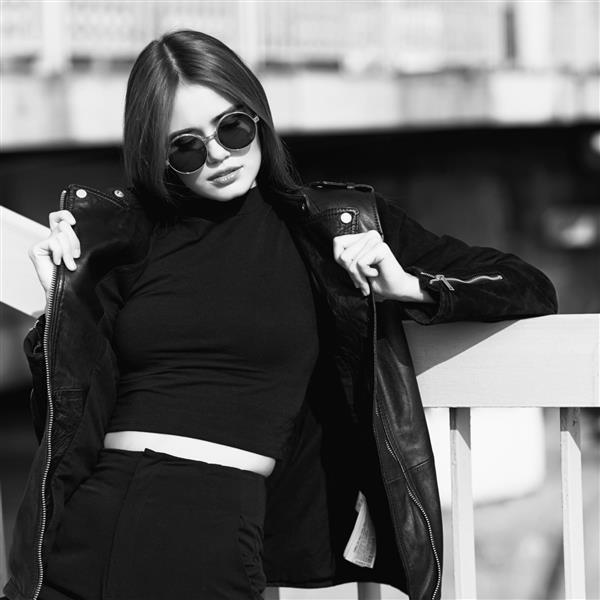 مدل مد عینک آفتابی و ژاکت چرمی مشکی در فضای باز تصویر سیاه و سفید