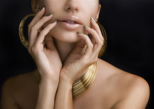لب های زیبای زنانه با رژ لب براق طلایی شیک و دست ها با مانیکور طلایی و جواهرات طلایی در زمینه تیره آرایش مد زیبایی مراقبت از ناخن