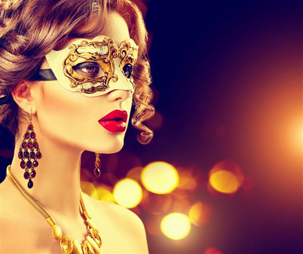 زن مدل زیبایی که ماسک کارناوال بالماسکه ونیزی را در مهمانی روی پس زمینه تیره تعطیلات با درخشش جادویی پوشیده است جشن کریسمس و سال نو خانمی جذاب با آرایش و مدل موی عالی