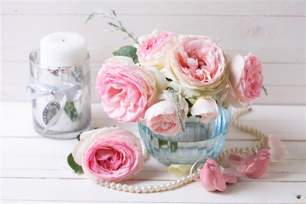 گل های رز صورتی در گلدان آبی روی زمینه چوبی نقاشی شده سفید تمرکز انتخابی