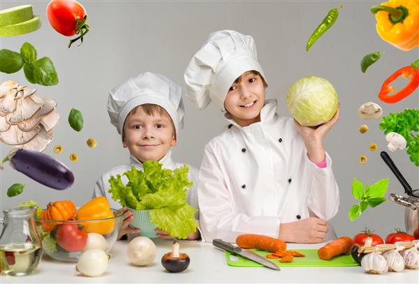 دو کودک خندان - آشپز کنار میز با سبزیجات پرنده در دست