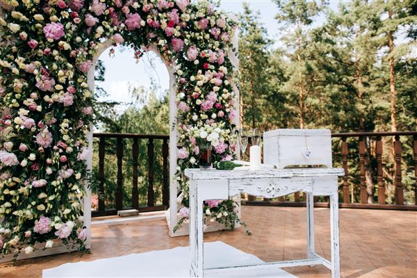 طاق برای مراسم عروسی تزئین شده با گل های تازه در یک جنگل کاج