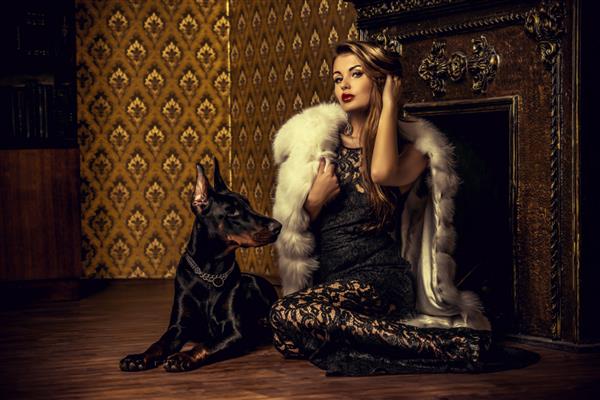 زن زیبا با جواهرات گرانبها و کت خز که کنار شومینه با سگش نشسته است فضای داخلی کلاسیک زیبایی مد