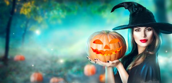 جادوگر هالووین با کدو تنبل حک شده و چراغ های جادویی در جنگلی تاریک زن جوان و زیبای متعجب با کلاه جادوگر و لباس کدو تنبل در دست دارد طراحی هنری جشن هالووین گسترده