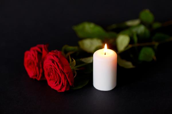 مفهوم تشییع جنازه و سوگواری - گل رز قرمز و شمع سوزان روی پس زمینه سیاه
