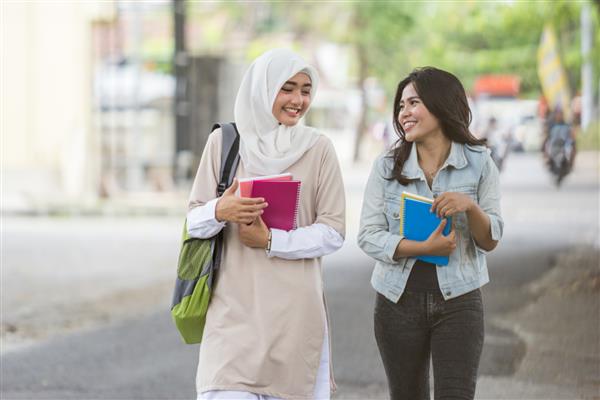 دو دوست دانشجوی آسیایی خوشحال در حال قدم زدن در محوطه دانشگاه