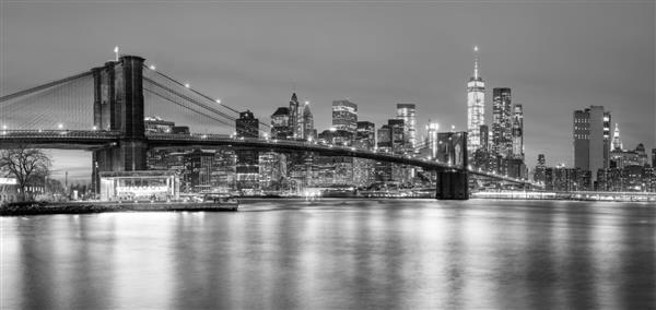 نمای پانوراما از پل بروکلین و خط افق منهتن پایین در شهر نیویورک در شب با روشنایی شهر ایالات متحده آمریکا رنگ سیاه و سفید