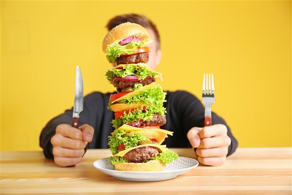 مردی در حال خوردن همبرگر بزرگ سر میز