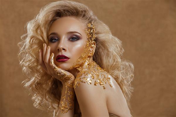 یک زن زیبا موهای مواج بلوند آرایش رنگ طلا جواهرات طلا مدل مد زیبایی پرتره کلوزآپ پوست تمیز الگوی بدنه طلایی در استودیو بر روی پس زمینه طلایی عکس گرفته شده است