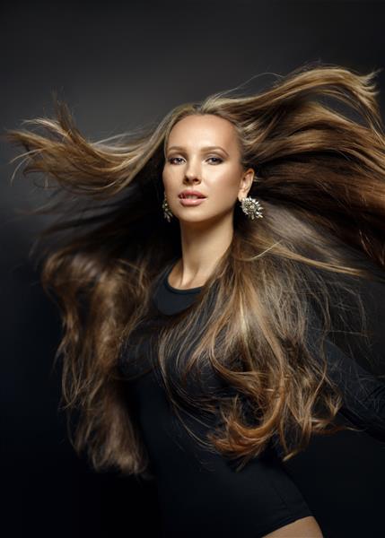 پرتره نزدیک از یک زن جوان زیبا با موهای براق طبیعی سالم در حال پرواز و زیبا روی پس زمینه سیاه مدل مد بالا و زیبا مدل موی شیک سالنی