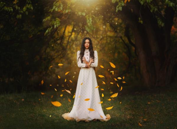 زن فانتزی عکاسی هنری گوتیک جادو می آفریند نور الهی روشن برگ‌های زرد پاییزی اوج می‌گیرند و در باد در اطراف شاهزاده خانم پری می‌چرخند خانم جادوگر لباس بلند سفید درختان سیاه جنگلی تاریک