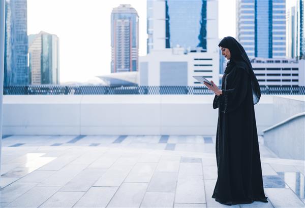 زن تاجر مسلمان عرب که در یک جلسه در فضای باز روی تبلت کار می کند بانوی تاجر عربستانی یا اماراتی با پوشیدن عبایا