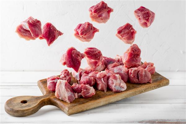 معلق شدن تکه های گوشت روی تخته برش تکه های گوشت خوک خام یا گاو در هوا آماده شدن برای پخت و پز