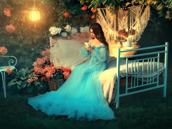 آثار هنری شاهزاده خانم افسانه روی تخت قدیمی نشسته است زن فانتزی که فنجانی در دست دارد و در حال نوشیدن چای است موهای موج دار بلند لباس لاکچری آبی پس زمینه گل های شکوفه لامپ قدیمی ملکه زن فانتزی