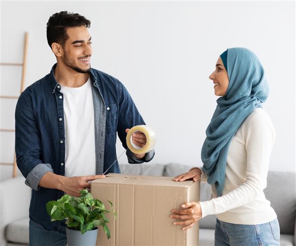 زوج زیبای جوان مسلمان در حال حرکت به خانه جدید بسته بندی وسایل خود استفاده از نوار و جعبه های کاغذی فضای کپی زن و شوهر خوشبخت خاورمیانه در حال تغییر آپارتمان تغییر مکان مفهومی