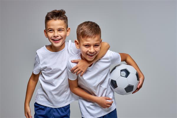 پسر بچه ها به طور حرفه ای برای ورزش فوتبال شرکت می کنند یکدیگر را در آغوش می گیرند سرگرم می شوند به دوربین لبخند می زنند توپ را در دست می گیرند پرتره ایزوله