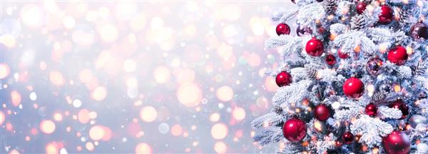 پس زمینه تعطیلات انتزاعی - درخت کریسمس برفی با بابل های قرمز با چراغ های غیر متمرکز براق