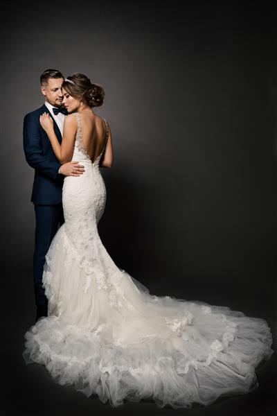 زوج عروسی عروس زیبا با لباس سفید با دم قطار بلند داماد زیبا در حال بوسیدن پرتره استودیو رمانتیک
