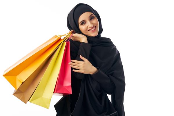 زن مسلمان زیبا با لباس مشکی عرب با لباس حجاب با بسته هایی در دست روی زمینه ای روشن