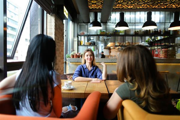 زنان اروپایی در یک کافه دنج نشسته اند لبخند می زنند و قهوه می نوشند مفهوم دوستی و زندگی شهری