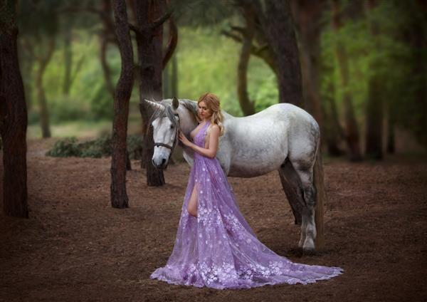 پری با لباس بنفش شفاف با قطاری بلند - اسب شاخدار را گرفت اسب جادویی و درخشان دختر بلوند در حال قدم زدن با پگاسوس در جنگل عکاسی هنری