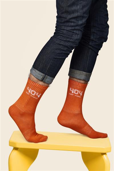 عکس بریده شده از پاهای مردی با شلوار جین آبی تیره که روی چهارپایه زرد باقی مانده است جوراب نارنجی است که روی پاهایش نوشته 404 یافت نشد عکس در پس زمینه بژ گرفته شده است