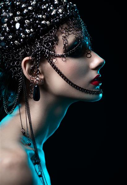 پرتره زن سبزه جذاب با روسری طراح با زنجیر که در پس زمینه تیره استودیو ژست گرفته است