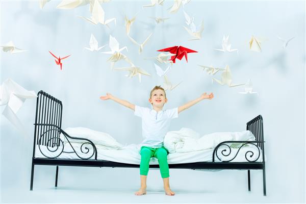 پسر کوچولوی بامزه ای که روی تختش نشسته و پرندگان کاغذی آن را احاطه کرده اند دنیای رویا