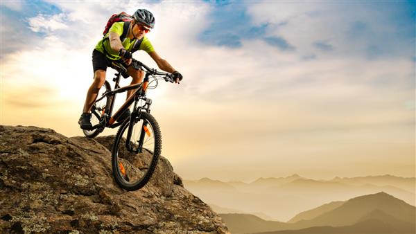 دوچرخه سواری دوچرخه سواری در پایین صخره در طلوع خورشید در کوه های زیبا در پس زمینه کانسپت دوچرخه سواری اسپرت و اندرو