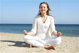 زن در حال مدیتیشن و یوگا در ساحل دریا با لباس سفید ویژه پوستر دیواری سالن‌های یوگا، کلینیک‌های زیبایی و دکوراسیون اتاق استراحت