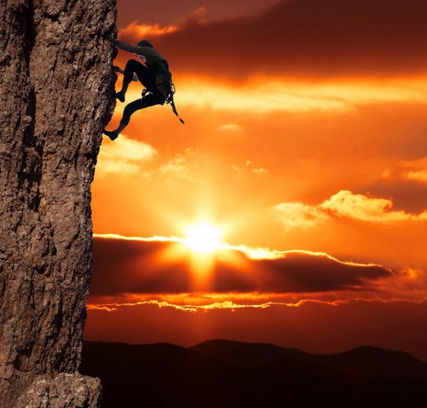 دختری در حال بالا رفتن از صخره در پس زمینه غروب خورشید