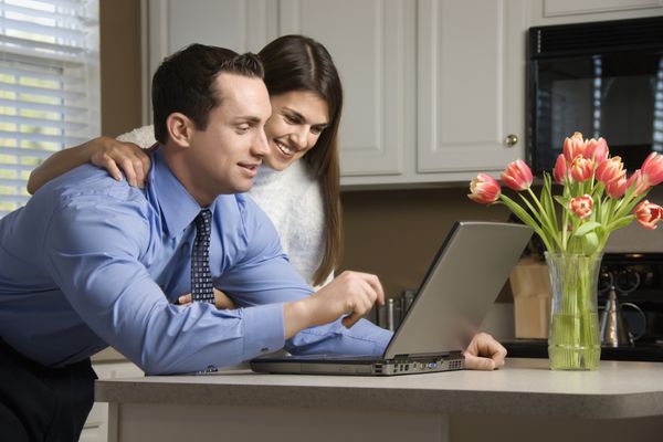 زوج قفقازی در آشپزخانه با قهوه که به لپ تاپ نگاه می کنند