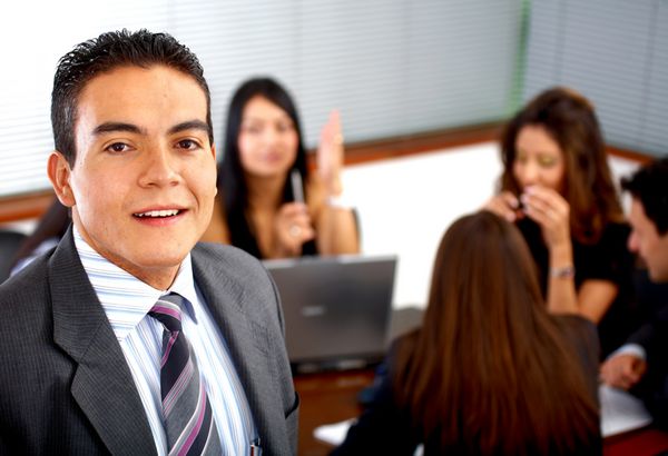 مرد تاجری که در طول یک جلسه اداری تیمی را رهبری می کند لبخند می زند