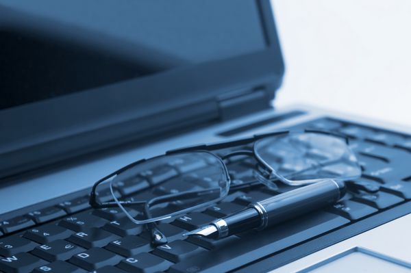 یک جفت عینک و یک خودکار روی لپ‌تاپ روی آبی نماد کسب و کار کار در دفتر تمرکز نرم