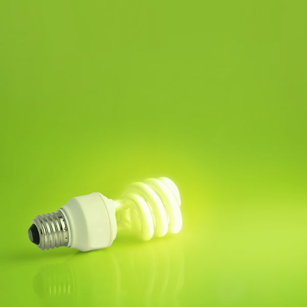 نمایشی پر جنب و جوش از یک لامپ کم مصرف مدرن که در پس زمینه ای سبز رنگ روشن شده است فضای کپی فراوان ایده آل برای محیط زیست مفاهیم انرژی یا تخیل و بازاریابی
