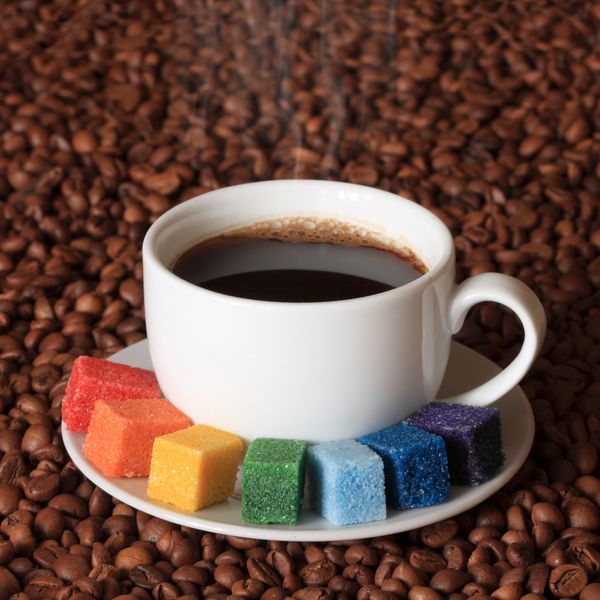 قهوه برای یک هنرمند در حال سیگار کشیدن فنجان قهوه با شکر رنگارنگ در پس زمینه دانه های قهوه