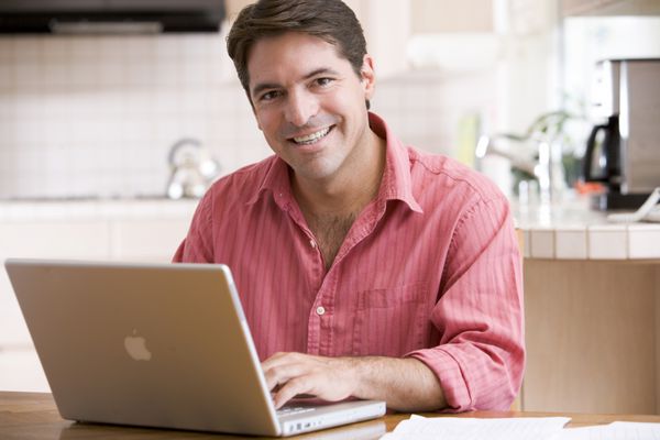 مردی در آشپزخانه با استفاده از لپ تاپ در حال لبخند زدن