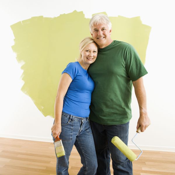 زن و شوهر میانسال جلوی دیوار مشغول رنگ آمیزی سبز هستند