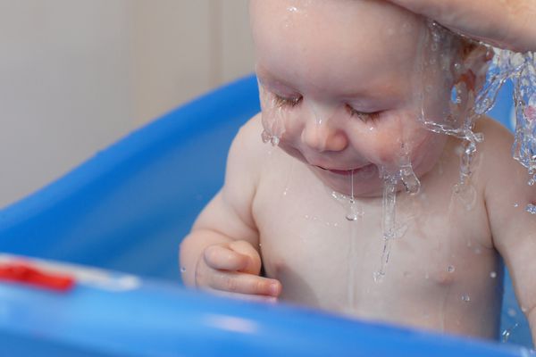 پسر بچه بامزه ای که هنگام حمام کردن روی سرش آب می ریزد چهره ای خنده دار می کند