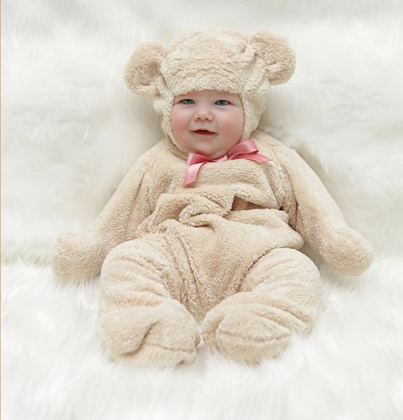 کودک در لباس خرس عروسکی که روی پس زمینه سفید نشسته است