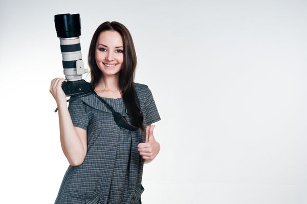 دختر خندان با دوربین حرفه‌ای که شست را بالا می‌گیرد عکس استودیویی