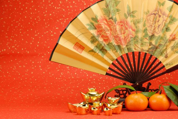 تزیین سال نو چینی - پنکه سنتی با شمش طلا و نارنجی در زمینه جشن