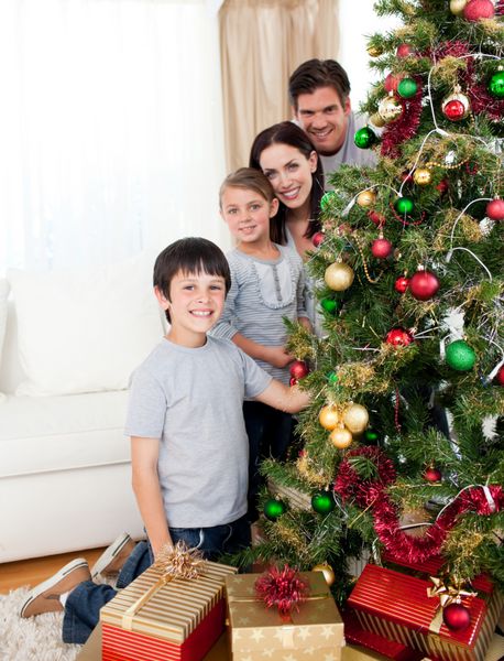 خانواده خوشبختی که درخت کریسمس را با گل و هدایا در اتاق نشیمن تزئین می کنند