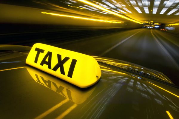 یک تاکسی با سرعت بالا در بزرگراهی در یک منطقه شهری با تابلوی تاکسی روشن در بالای سقف آن