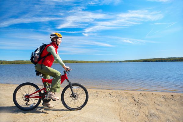 زن جوان خندان دوچرخه سواری در نزدیکی دریاچه