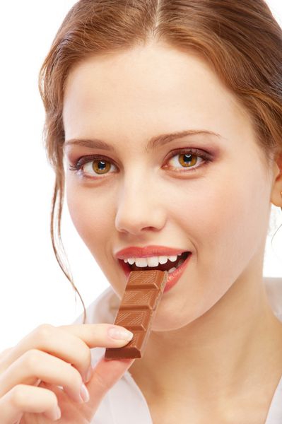زن جوان زیبا شکلات را گاز می گیرد جدا شده در پس زمینه سفید