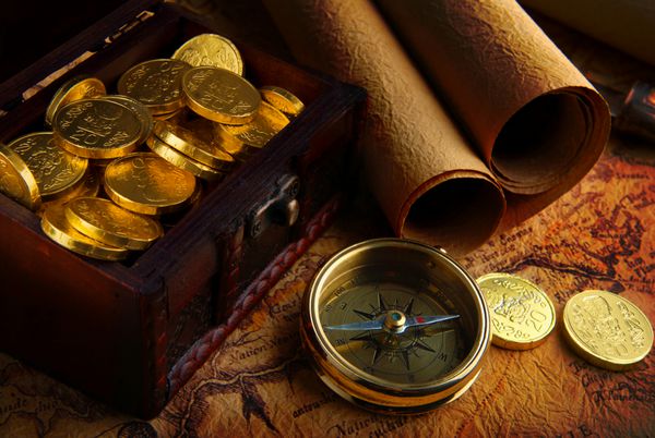قطب نما برنجی قدیمی روی یک نقشه بسیار قدیمی با صندوقچه گنج پر از سکه های طلایی قرار گرفته است
