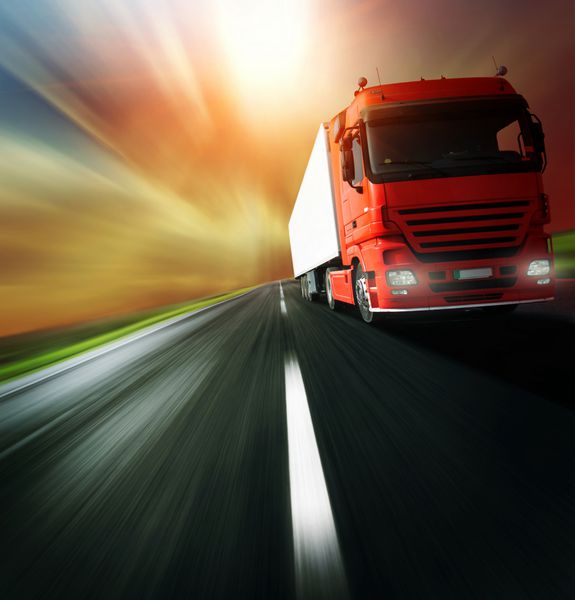 کامیون قرمز در جاده آسفالت تار در پس زمینه آسمان ابری