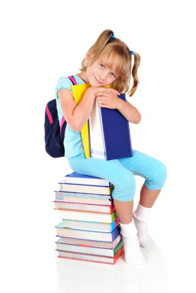 دختر مدرسه ای کوچک روی انبوهی از کتاب ها نشسته است